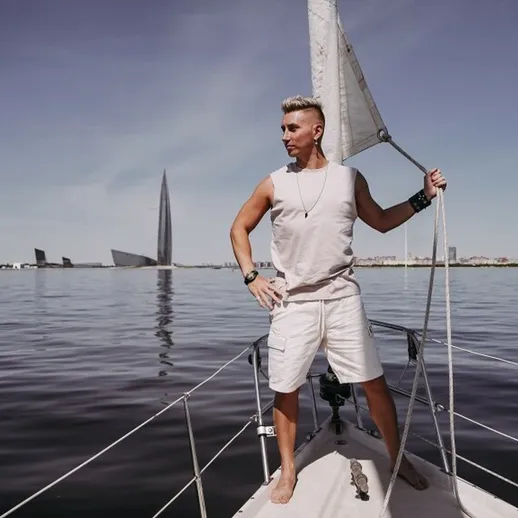 Мужчина стоит на носу парусника, наслаждаясь спокойствием на воде у берега крупного города в ясный день