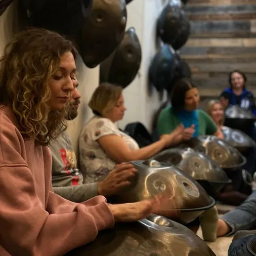 Группа людей играет на хэндпанах в уютной комнате во время музыкального занятия