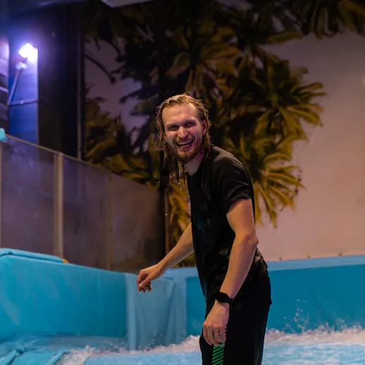 Молодой человек катается на доске в крытом аквапарке, наслаждаясь волной в вечернее время