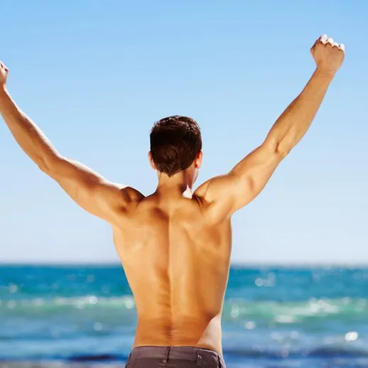 Мужчина с поднятыми руками на пляже наслаждается днем у моря во время солнечной погоды