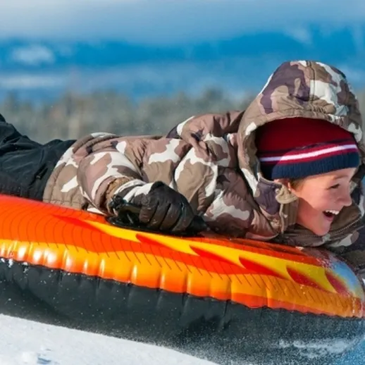Девочка катается на санках с горки в зимнем лесу, окруженная снежными пушистыми деревьями и ясным небом