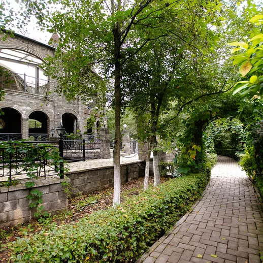 Зеленая аллея в парке рядом с историческим зданием, окруженная деревьями и кустарниками