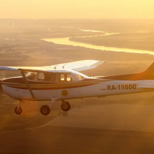 Самолёт Cessna RA-1980C летит над живописным заливом на закате, освещая окрестности мягким светом