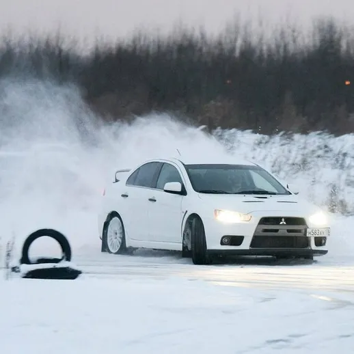 Белый спортивный автомобиль на заснеженной дороге, демонстрирующий дрифт в зимних условиях на фоне зимней природы