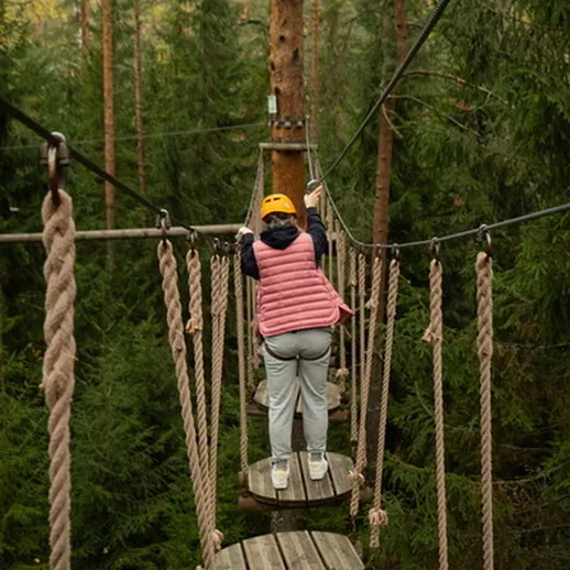 Подросток в ярком жилете проходит по канатному парку в лесу, наслаждаясь активным отдыхом и природой
