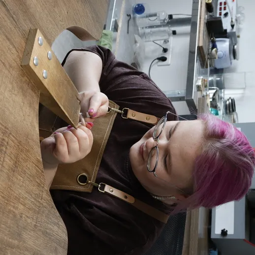 Женщина с фиолетовыми волосами занимается деревообработкой в мастерской, создавая уникальный элемент дизайна