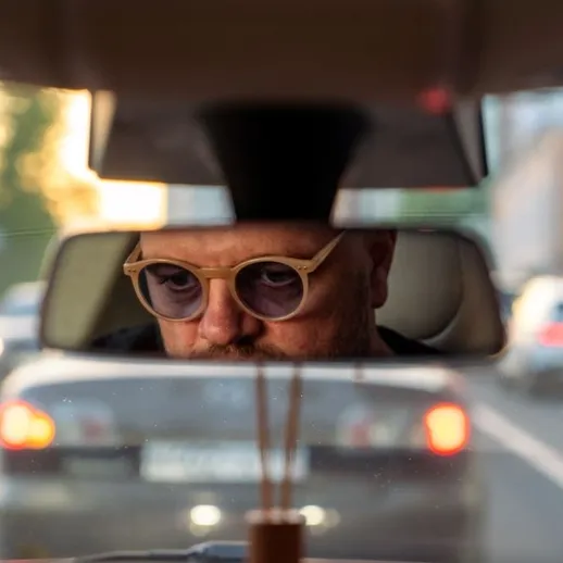 Водитель в очках за рулем автомобиля в городском потоке в солнечный день