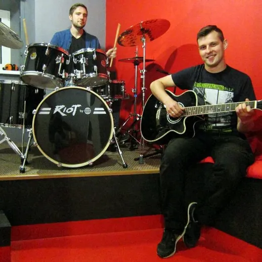 Музыканты играют на гитарах и барабанах в студии репетиций в вечернее время