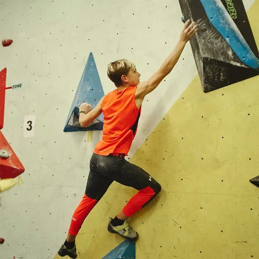 Молодой альпинист занимается скалолазанием в спортзале с яркими стенами в осенний день