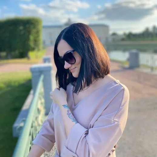 Женщина с тёмными волосами и солнцезащитными очками на мосту в парке в ясный день