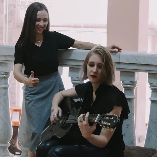 Две девушки играют на гитаре в историческом здании во второй половине дня
