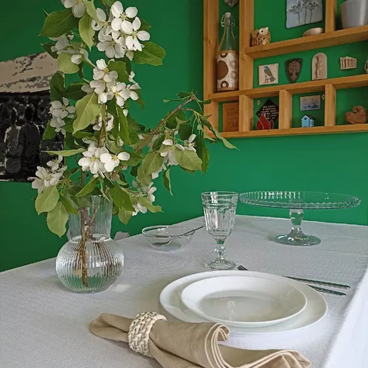 Цветы яблони в вазе и столовая сервировка в современном интерьере на зеленом фоне