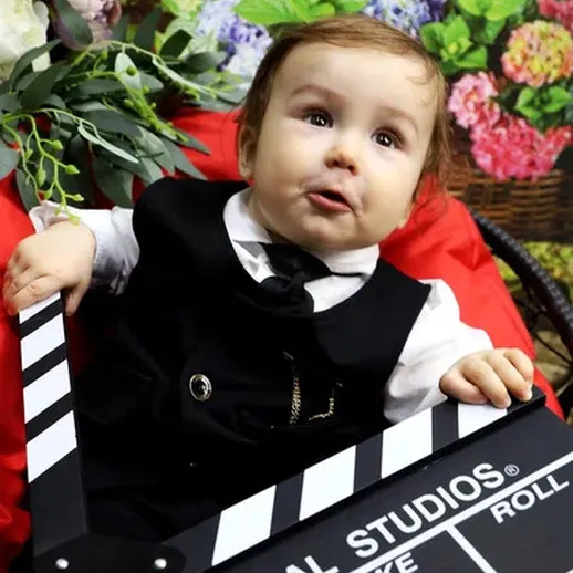 Малыш в черном костюме держит клепку на фоне цветущих растений в студии