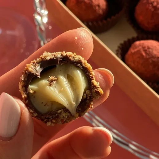 Крупный план шоколадного трюфеля с начинкой, стоящего на розовом фоне рядом с коробкой с другими сладостями