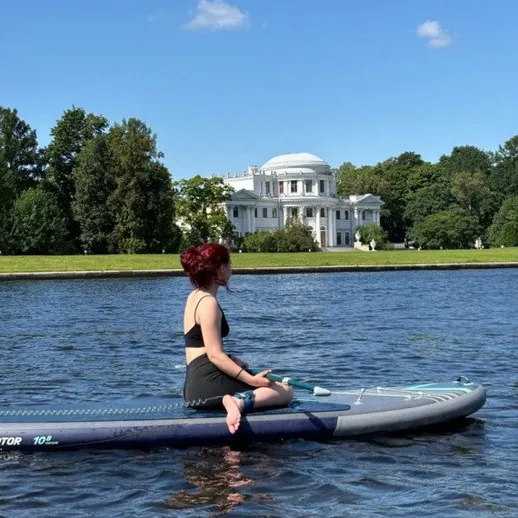 Женщина на вечернем паддлборде на озере рядом с историческим зданием в солнечный день