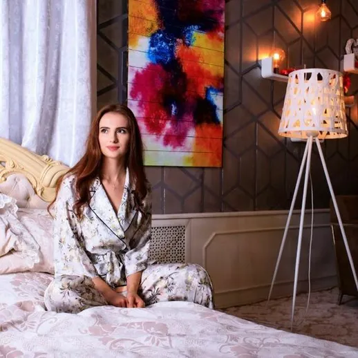 Молодая женщина в пижаме сидит на кровати в уютной спальне с оригинальным декором и мягким освещением