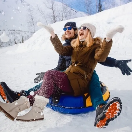 Счастливая пара катится на тюбинге по снежному склону в зимнем курорте под ярким солнечным небом