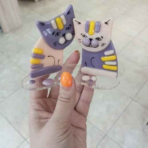 Забавные фигурки котиков в руках, украшенные яркими цветами, в уютном интерьере магазина