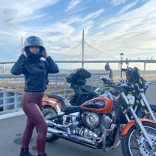 Модель позирует рядом с мотоциклом в солнечный день на набережной города