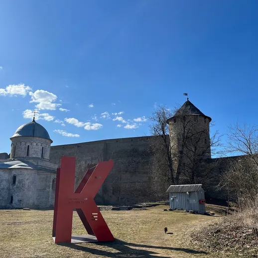 Красная буква K на фоне старинной крепости и голубого неба в историческом центре города