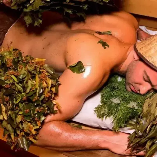 Парень в бане с вениками из березы и еловыми ветками, отдыхает после процедур в традиционной русской бане