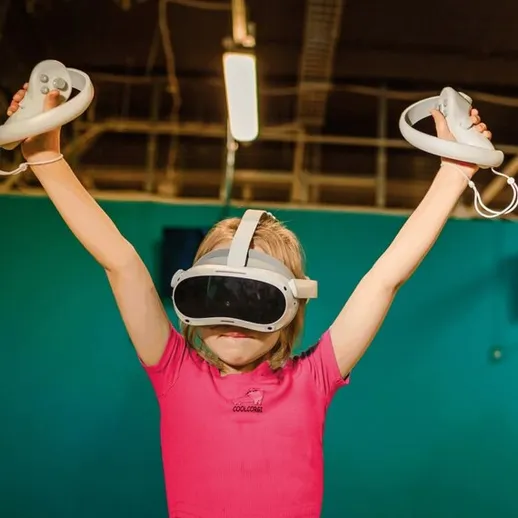 Девочка в виртуальной реальности радостно поднимает руки с контроллерами в игровом центре