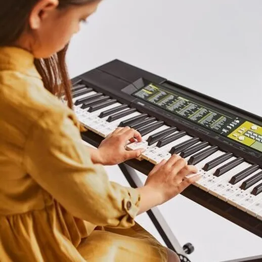 Девочка играет на синтезаторе в желтом платье в уютной комнате