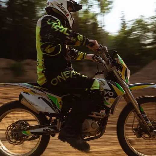 Мотоциклист в спортивной экипировке на внедорожном треке в лесу в солнечный день