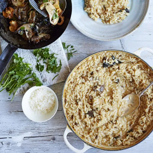 Вкусный ризотто с грибами и зеленью на деревянном столе в уютной кухне