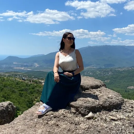 Женщина в длинной юбке и солнечных очках на скале с видом на горы и долины в ясный день