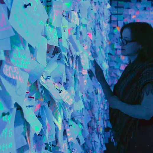 Женщина рассматривает светящиеся записки на стене в творческом пространстве