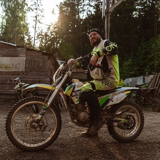 Мужчина на мотоцикле в лесу, подготовленный к езде, наслаждается вечерним светом и атмосферой активности