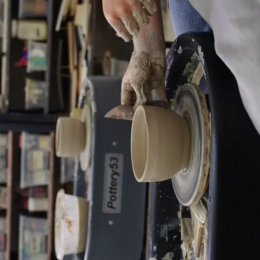 Создание глиняной кружки на гончарном круге в мастерской, наполненной инструментами и материалами