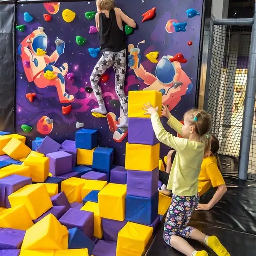 Дети занимаются скалолазанием в центре активного отдыха на тренажерах с мягкими блоками в выходной день