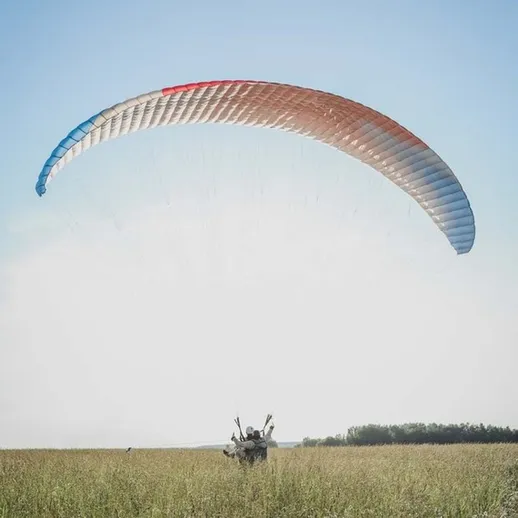 Парапланирист в полете над зеленым полем в ясный солнечный день