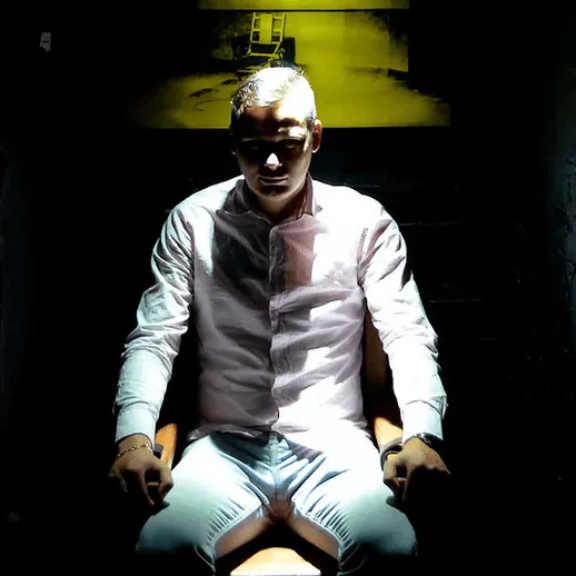 Человек в светлой рубашке сидит на стуле в темной комнате с приглушенным светом