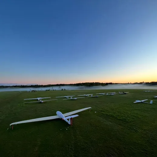 На рассвете легкие самолеты стоят на травяном поле возле аэродрома, создавая атмосферу покоя и ожидания