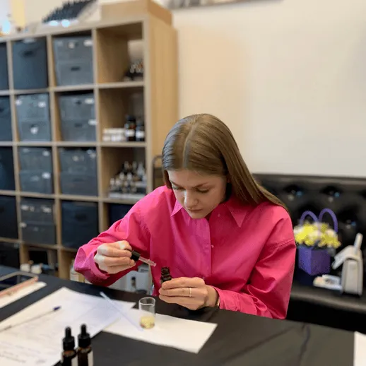 Девушка в розовой рубашке смешивает эфирные масла в лаборатории для создания натуральной косметики