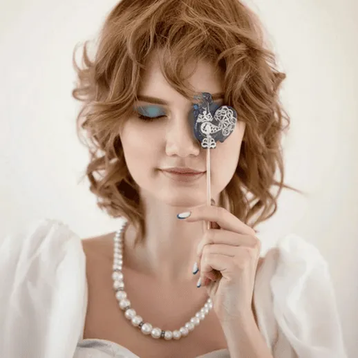 Молодая женщина в белом платье с маской, на фоне светлой стены, во время весёлого праздника или фотосессии