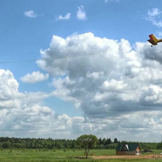 Летящий самолёт с буксируемым планером над зелёным полем в ясный день