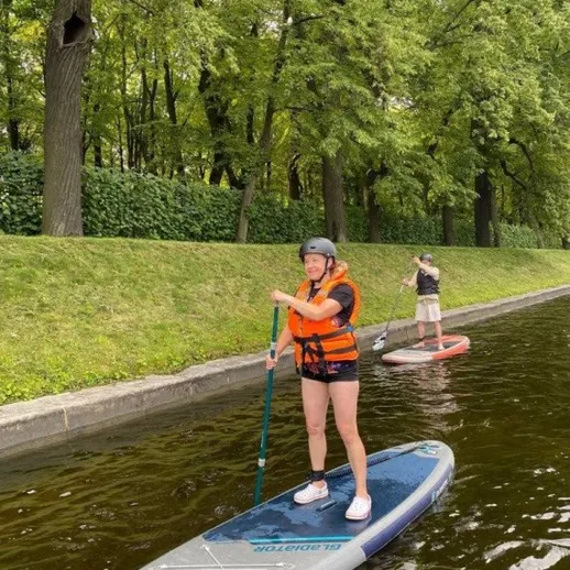 Женщина на сапборде в жилом районе, наслаждающаяся днем на воде до заката в зеленом окружении