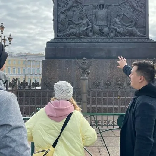 Группа туристов у памятника в центре города Санкт-Петербург, обсуждающие детали его архитектуры и истории