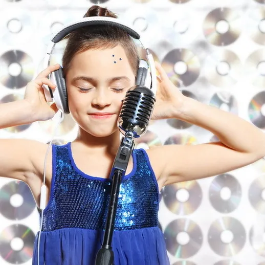 Девочка в блестящем платье держит микрофон и слушает музыку на фоне зеркальных дисков