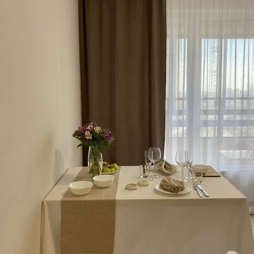 Уютный стол для ужина в светлой комнате с занавесками и цветами на столе