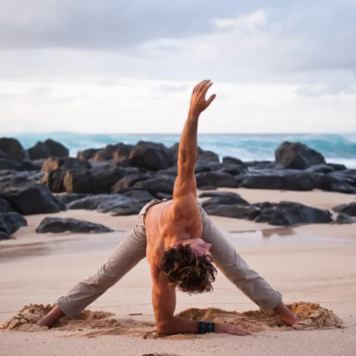 Йога на пляже во время заката: мужчина выполняет асану на песке у океана