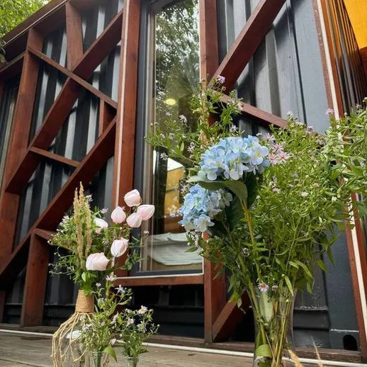 Цветы на деревянной веранде у стильного дома из контейнера в природном окружении