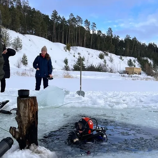 Подводное погружение дайверов в замерзшем озере среди зимних лесов