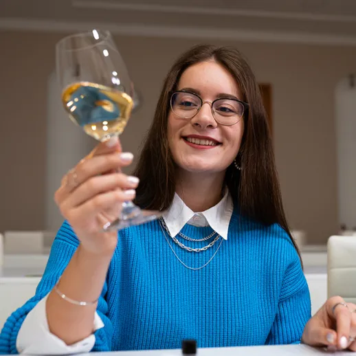 Молодая женщина в голубом свитере с бокалом вина на столе в уютном помещении