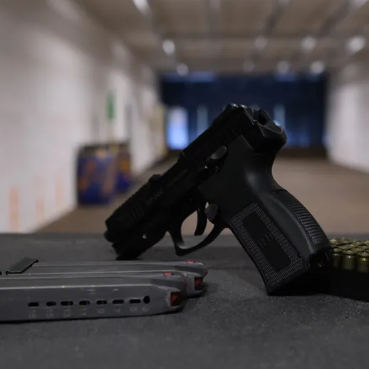 Пистолет и обойма на столе в тире, фон размытый, показывающий внутреннюю часть стрельбища