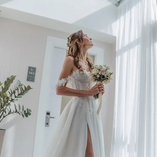 Свадебное платье и букет в руках невесты на фоне светлой комнаты